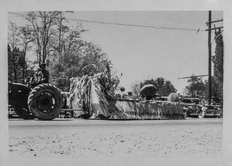 A float being pulled by a tractor. A couple children are riding, the boy is wearing cowboy gear.