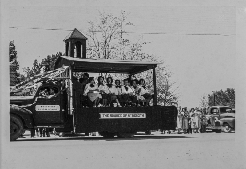 The Methodist Church's Sunday School float. Riding are a group of men and women who appear to be singing. The float is titled "The Source of Strength."