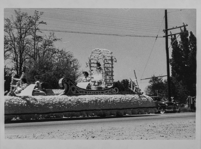 Several young ladies riding a float. The float is unidentified, but one of the ladies is holding a floral-covered plow.