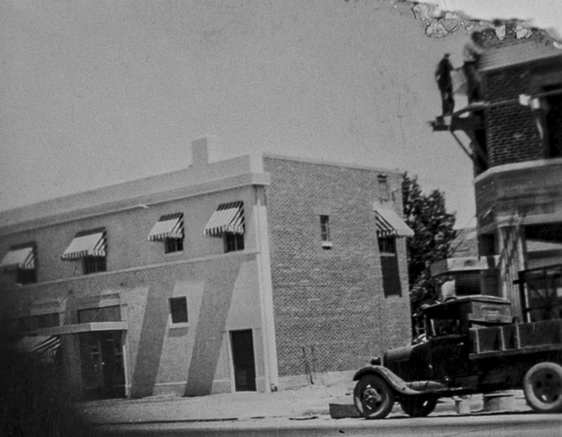 Slightly obscured view of a building, truck, and men working on the second floor