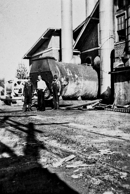 Three men pose in front the the old boiler at the Meridian Creamery.