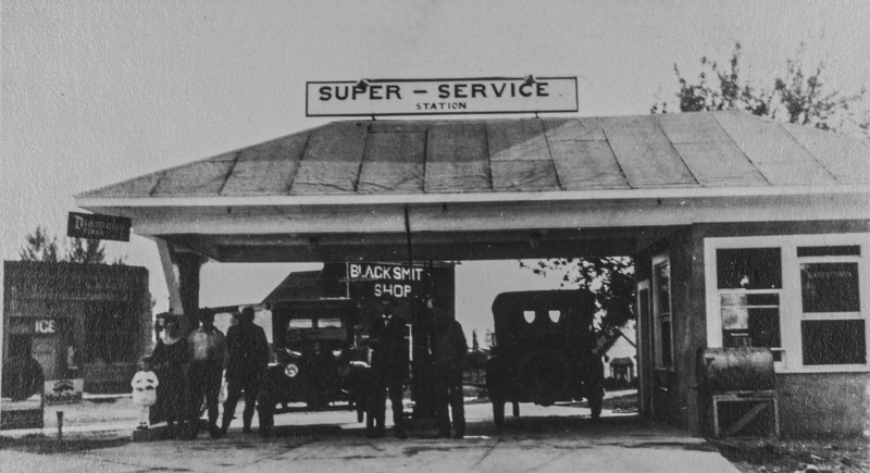 Close up shot of the service station, Broadway & E. 1st (Main St.), blacksmith shop in the back.