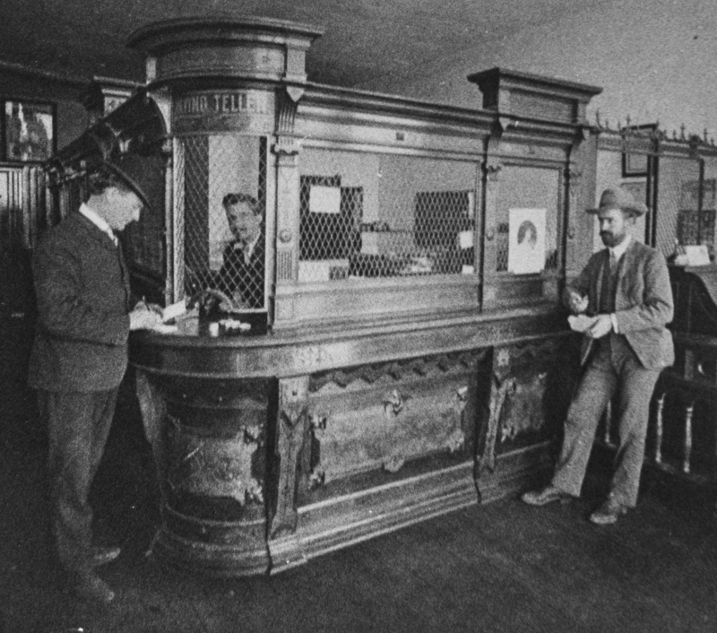 Inside the exchange bank, the picture shows the teller's cage and three gentleman.