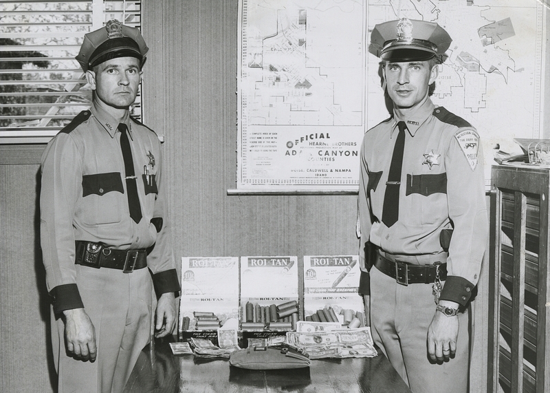 Police Chief Gene Hiner and Officer Charles Stuart show stolen money (cash, coins and deposit sack) taken from the Palamino Cafe in Ontario. Suspect was Edward Killingsworth. Money apprehended totaled $1,201.85. 