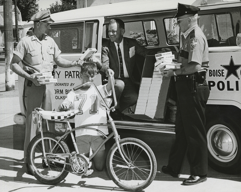 July 1968-The Idaho State Police and local authorities promote luminous safety tape for bicycles; Rayme Wilmot of Meridian is the child in front, in back (from left to right) are Gene Hiner, Carl Burt (Driver Improvement Division), and Bob Moran (safety official for Boise Police)