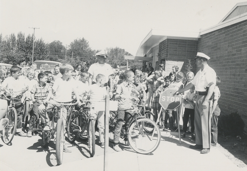 Police Chief Gene Hiner leads bicycle training course at Meridian grade school. Upon completing course, children issued bicycle safety certificates signed by Hiner and school principal Obed Dahl