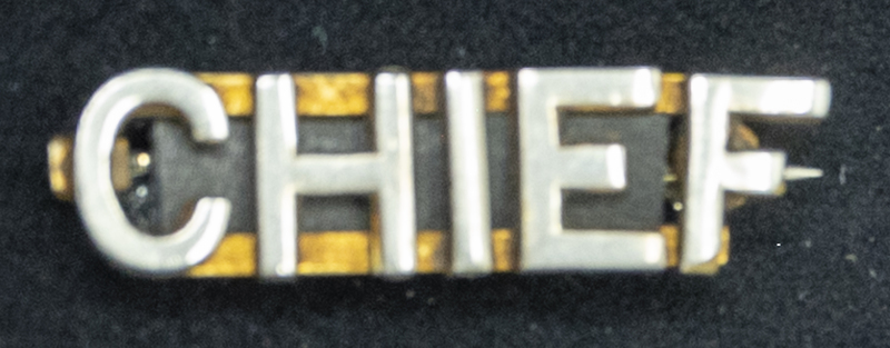 Gene Hiner Chief collar pin, the second part of his MPD collar pin set. The matching collar pin says "MPD." The MPD and Chief pins would be pined, one on each side of the shirt collar. Hiner would have worn this between 1963-1973. Part of the Gene Hiner Police Career Display presented to the MPD by Gene Hiner's family. 