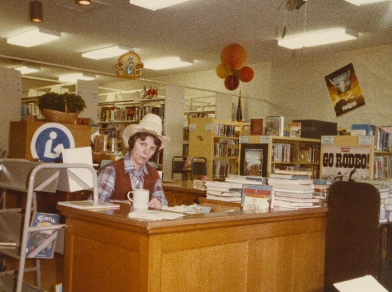 Pat works at the desk celebrating the library's Western theme by wearing a cowgirl hat. 