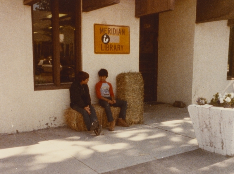 Ron and Ryan Ayde sit on hay bales outside the Meridian Library.