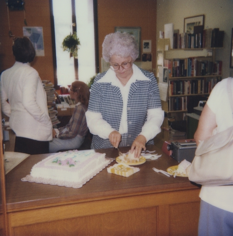 The Staff and Library Board got together to honor Librarian Evelyn. Evelyn is cutting the cake while Nancy and Denise talk in the background. 