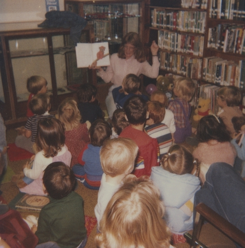 Librarian reads a bear story on Good Bear Day's Tea Party for Toddlers and Preschoolers. Some bears can be seen within the audience. 