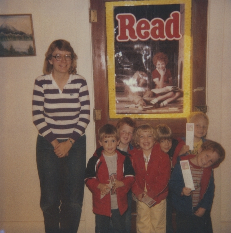 Children gather in front of a "Read" poster smiling as they show off their new bookmarks. 