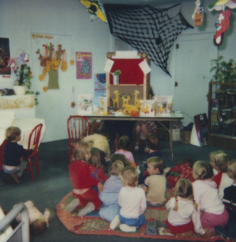 Children sit on the floor watching a Sesame Street puppet show. 